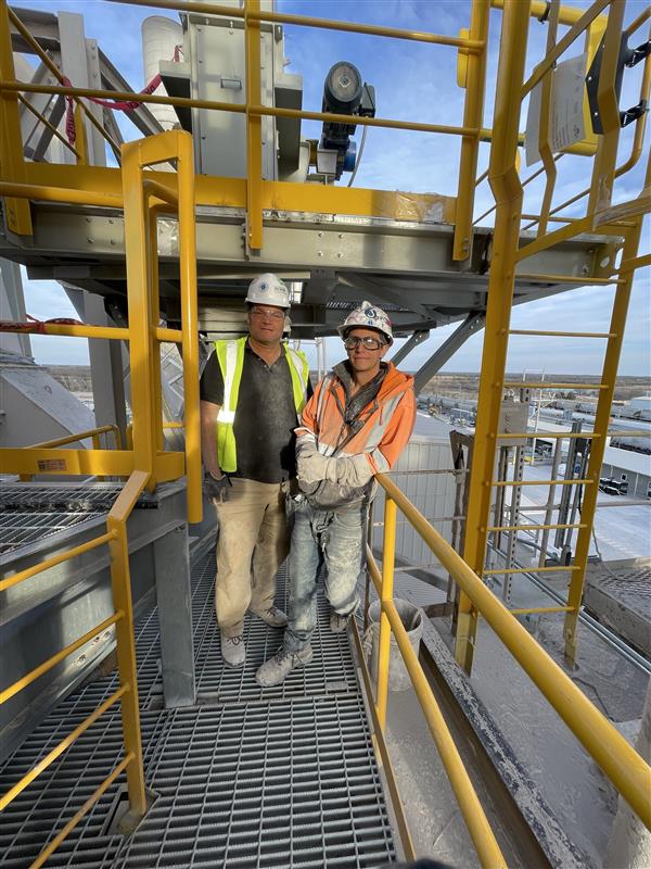 Two team members wearing safety equipment on an elevated industrial platform.